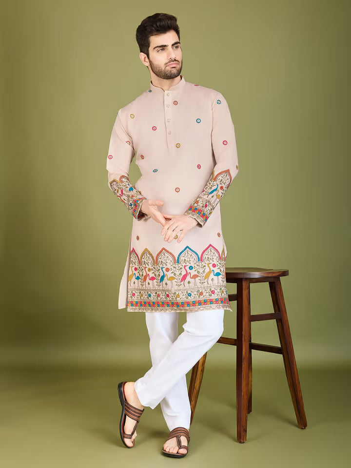 Man wearing a traditional embroidered kurta with white pants on a green background