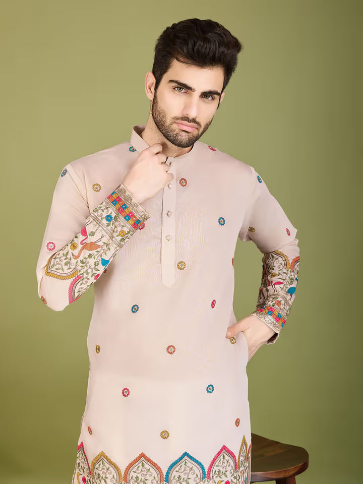 Man wearing a cream kurta with colorful embroidery on a green background