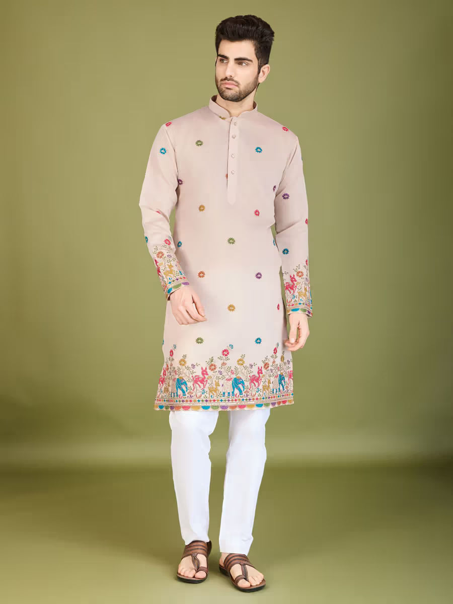 Man wearing a beige printed kurta with multicolor traditional patterns and white pants, standing against an olive green background.