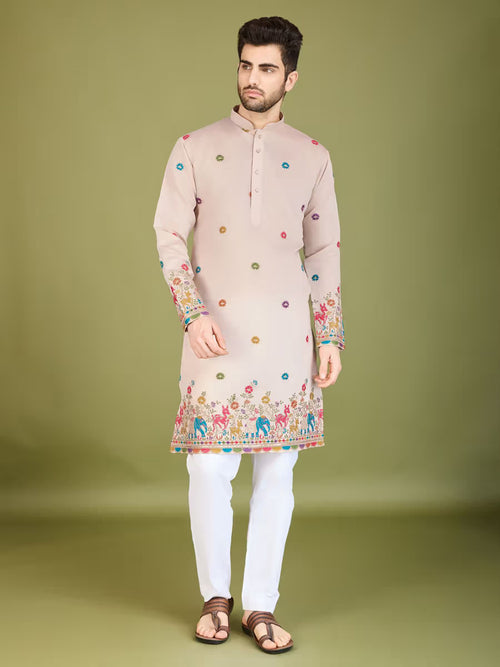 Man wearing a beige printed kurta with multicolor traditional patterns and white pants, standing against an olive green background.