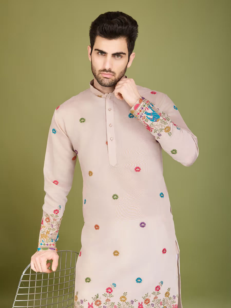 Man wearing a light-colored kurta with floral embroidery on a green background