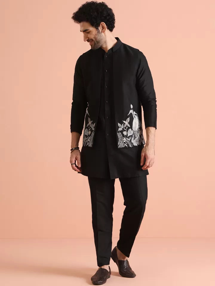 Man wearing a black kurta with white embroidery on a peach background