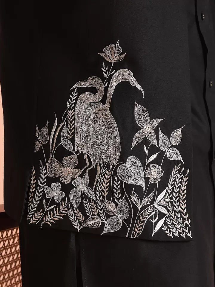 Black shirt with white embroidered design of a heron and floral elements.