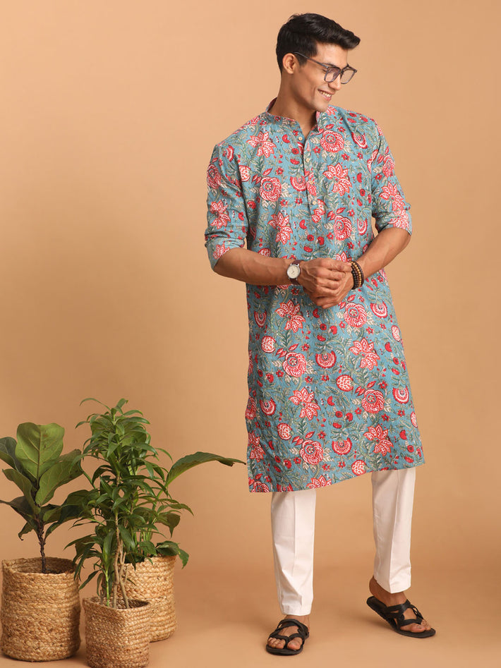 Man wearing a floral kurta with white pants standing against a beige background