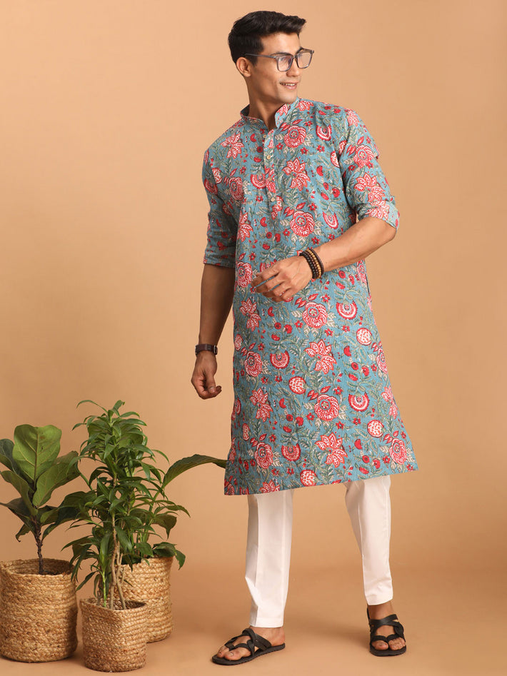 Man wearing a floral kurta with white pants against a beige background