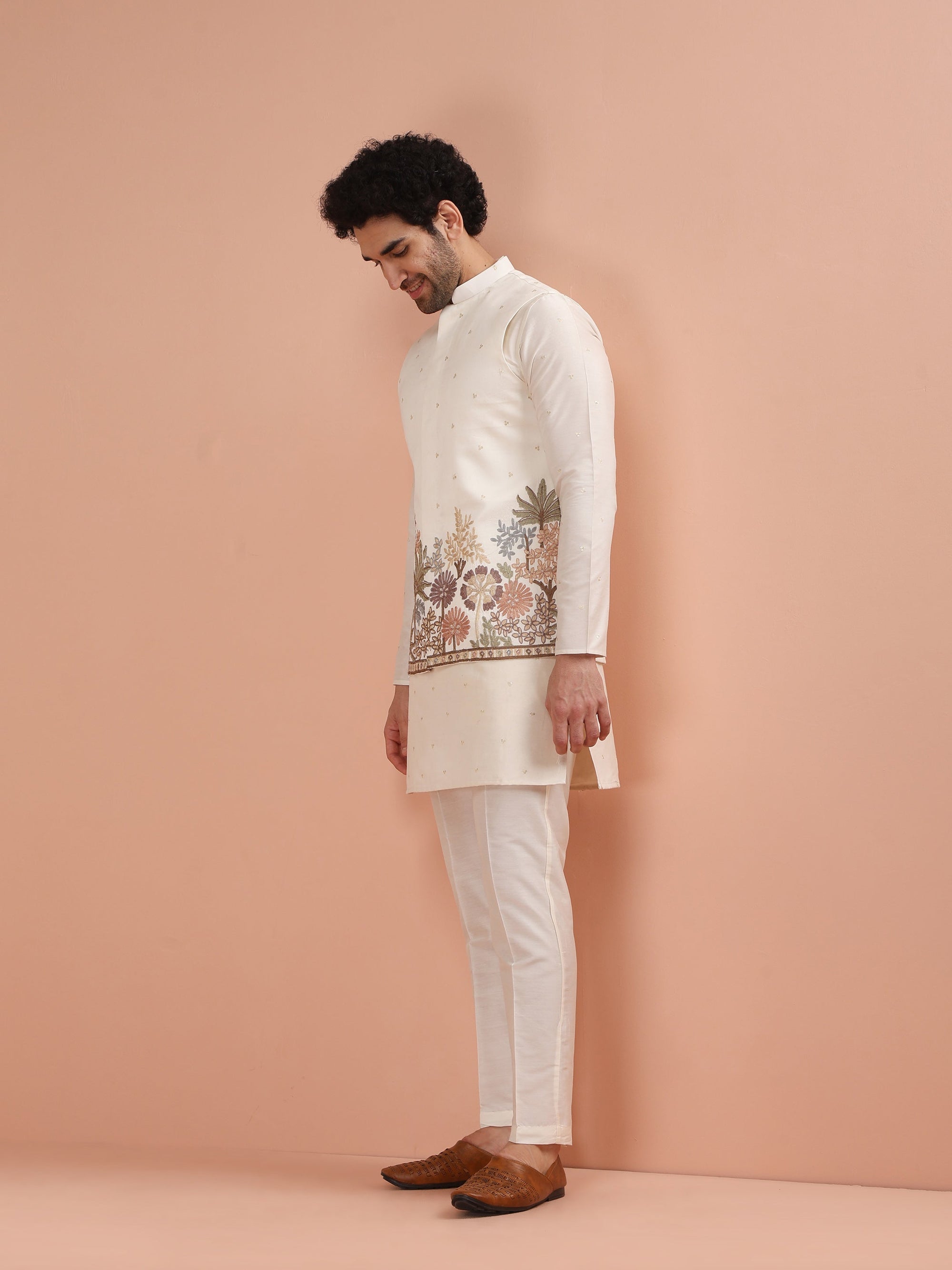 Man wearing a traditional embroidered kurta with white pants against a beige background