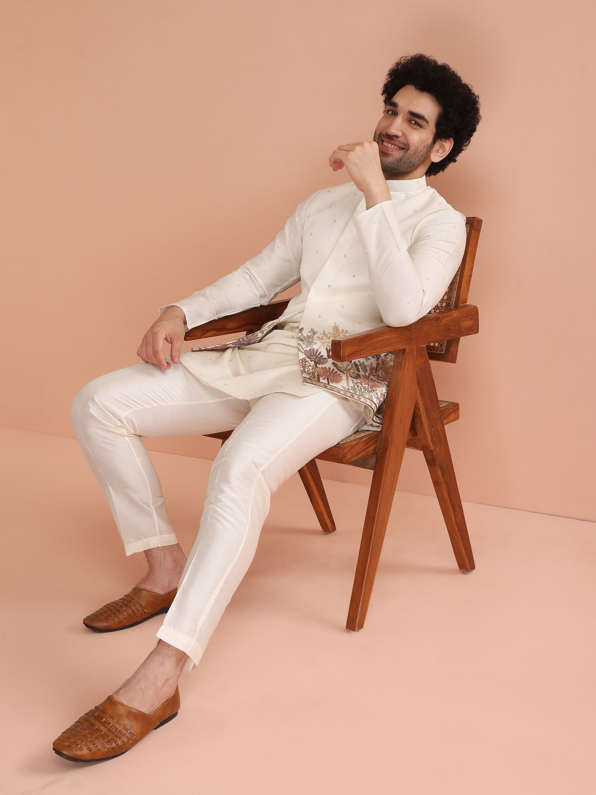 Man sitting on a wooden chair wearing a white outfit with a beige background