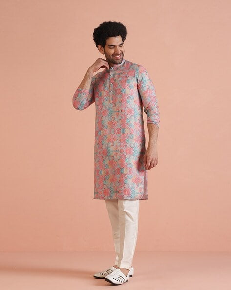 Man wearing a patterned kurta with white pants on a peach background