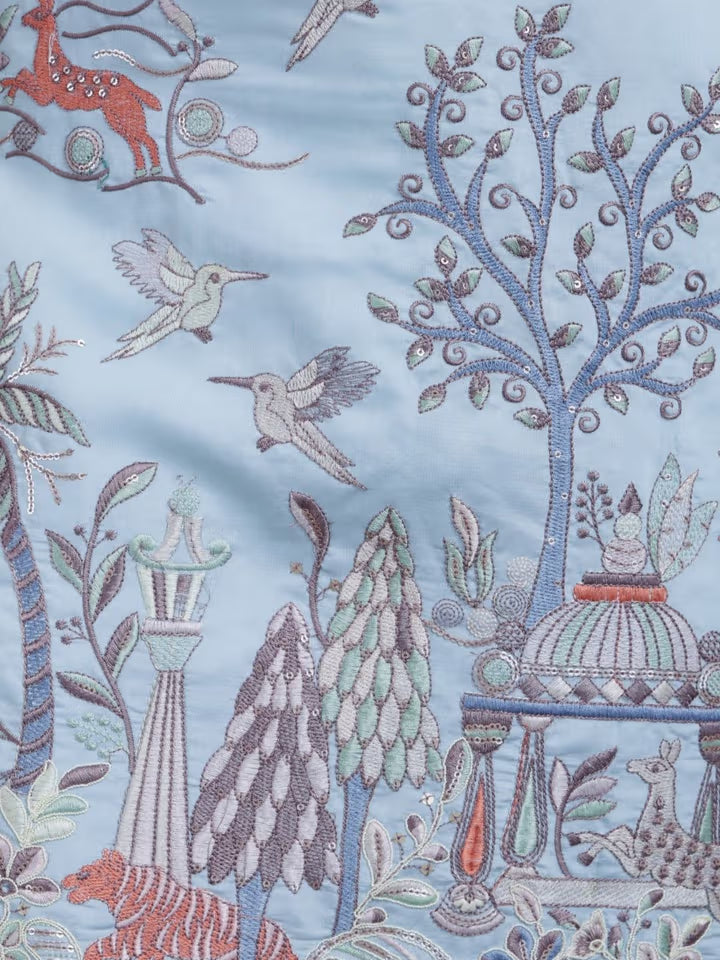 Embroidered fabric with intricate designs of trees, animals, and birds on a blue background.