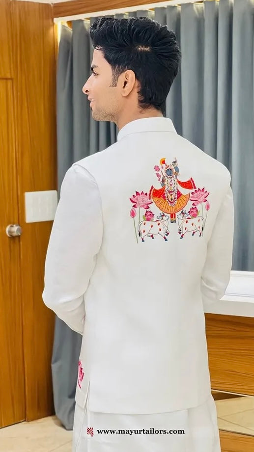 Man wearing a white embroidered kurta in a room with wooden door and gray curtains.