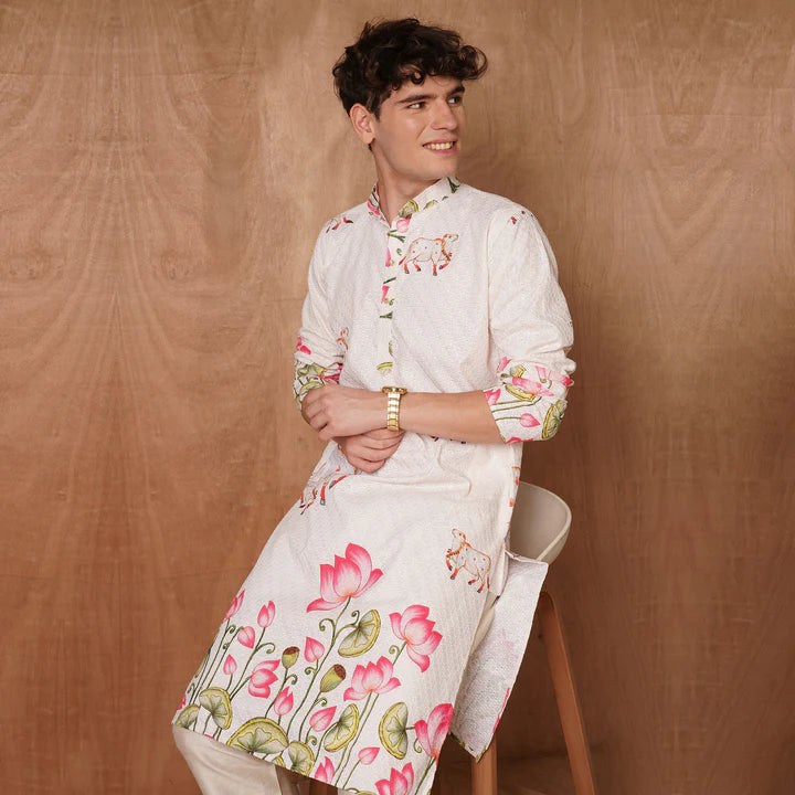 Person wearing a white kurta with floral patterns against a brown background