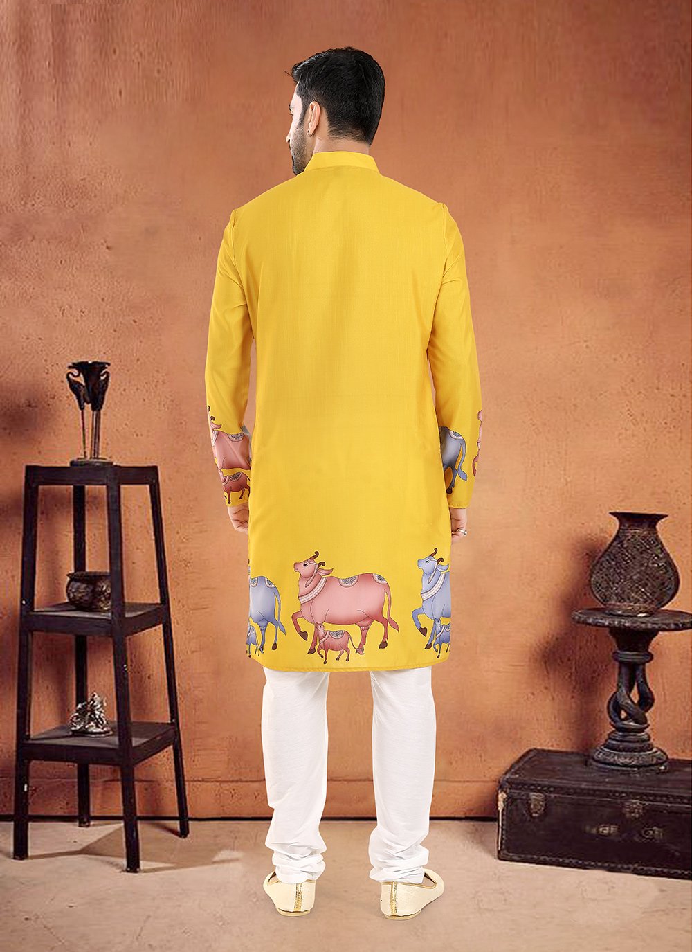 Man wearing a yellow kurta with animal prints in a room with decorative items.